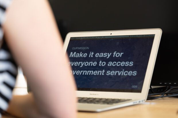A laptop screen reads "Our mission: make it easier for everyone to access government services"