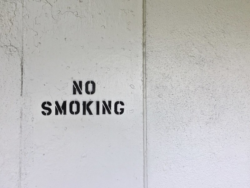A concrete wall with the words "No smoking" sprayed on using a stencil in black block capitals